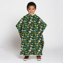 A young child wearing a dark green poncho-style blanket with a colorful cartoon dinosaur pattern, standing against a light gray studio background.