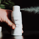 Samson's Haircare Volumizing Dry Shampoo Matte Powder front of white bottle being squeezed by a hand and powder coming from the nozzle view on a black background