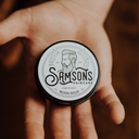 Samson's Haircare Beard Balm Original jar view from top of the jar, white circle label reads Samsons Haircare beard balm, being held in a hand