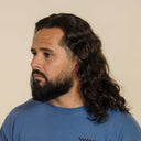 Man with long hair and beard wearing a blue shirt against a beige background